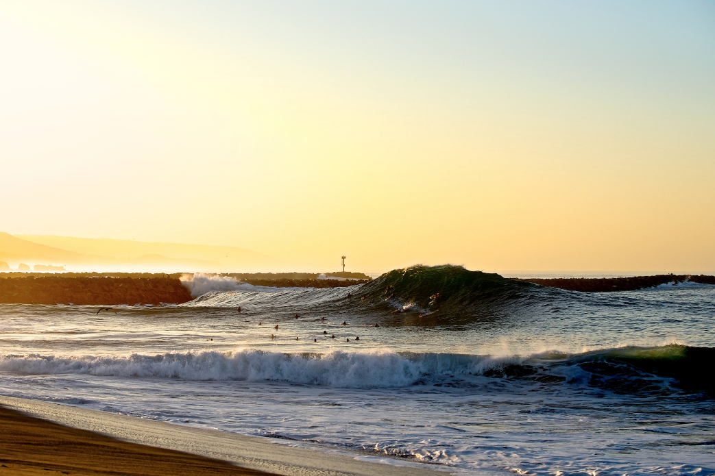 A massive, refracted peak towers over the assembled crowd of locals on during this late season dawn session at the Wedge.