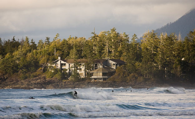 Surfers enjoy the cold waves on North Chesterman Beach with the cozy Wickaninnish Inn nestled in the background.
