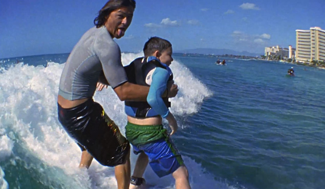 Kalani Robb teaches, through the Mauli Ola Foundation, a young boy afflicted by cystic fibrosis how to surf. Image: screenshot, Mauli Ola Foundation