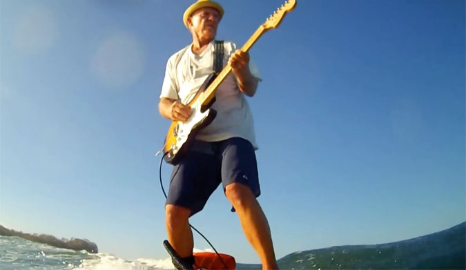 Guy playing guitar while surfing.