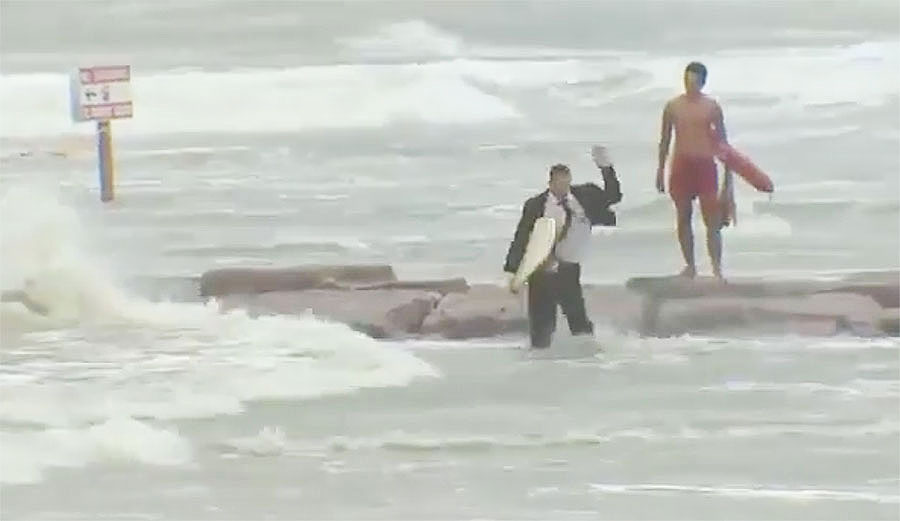 We have no idea what is going on here, but it's a man in a suit with a surfboard apparently attempting to surf during Hurricane Harvey.