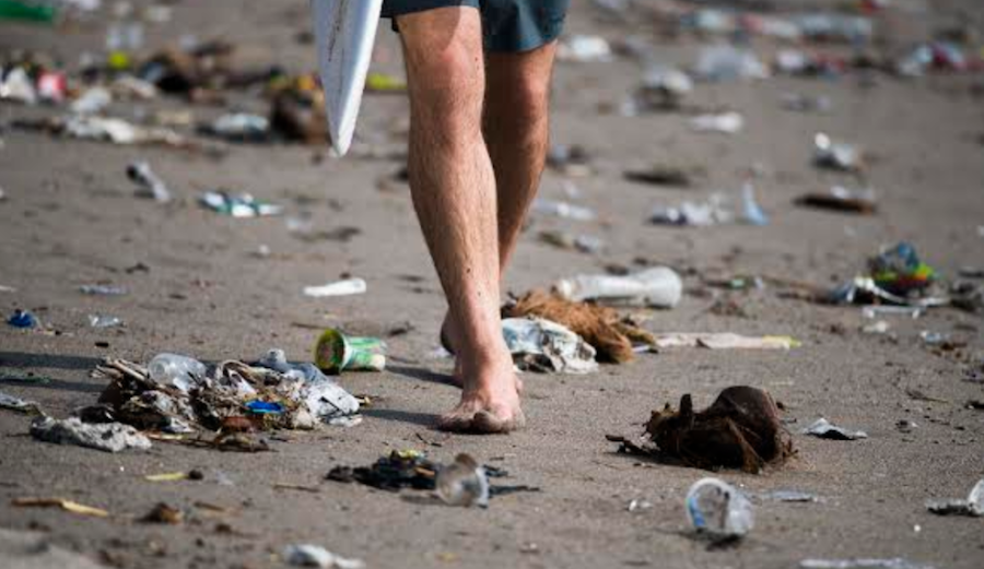 Trash in Bali as surfer walks beach.