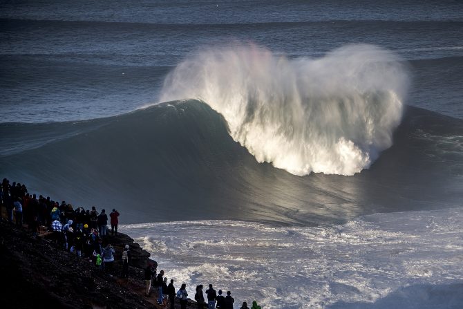 A big wave in Nazare, Portugal with crowds.