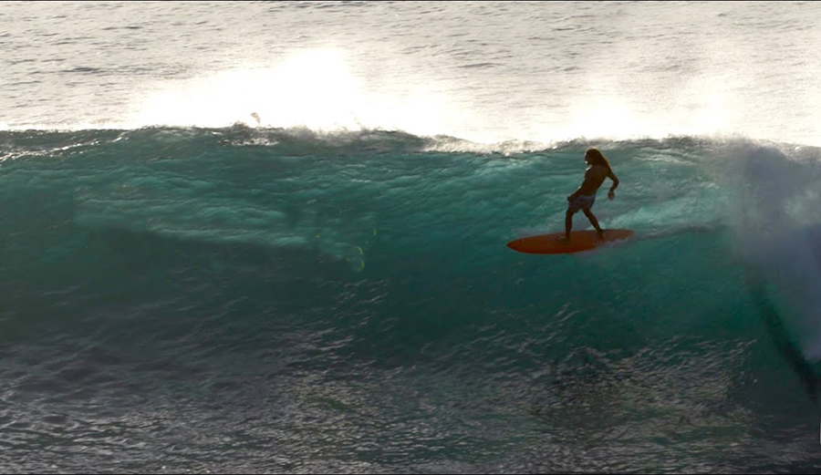 Surfer rides mid-length surfboard on big wave