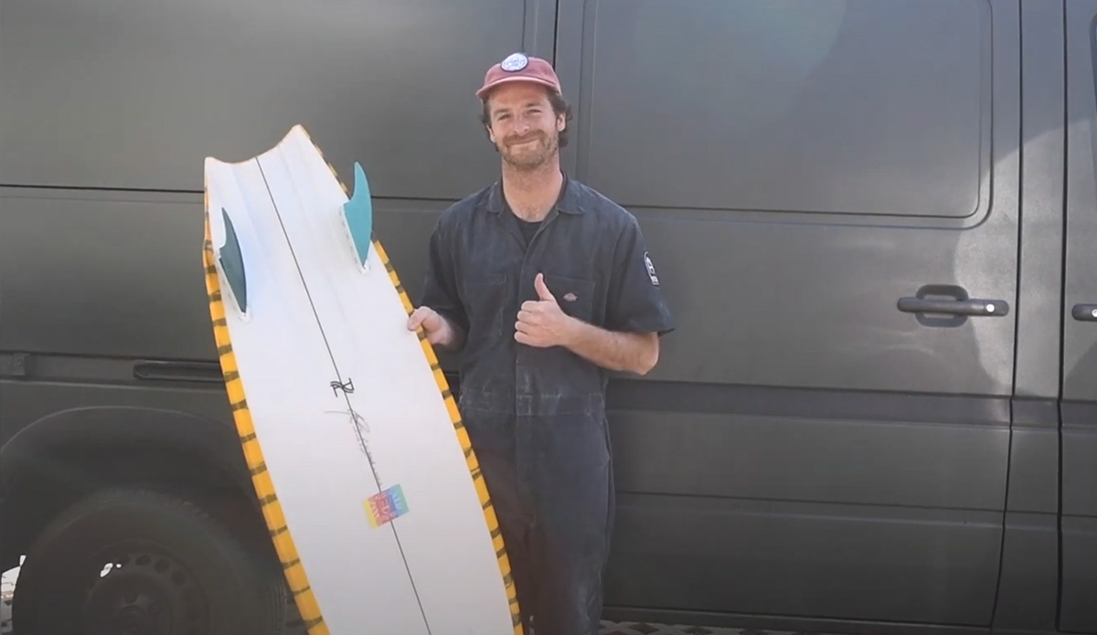 A man holds a twin fin surfboard in front of a van