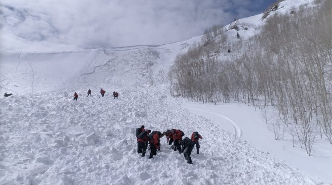 Rescue teams on a snowy slope work to excavate a lost person.