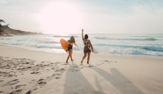 elizeu dias via unsplash two women surfers on the beach for mom
