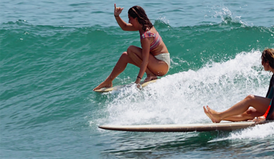 A girl throws a shaka while longboarding