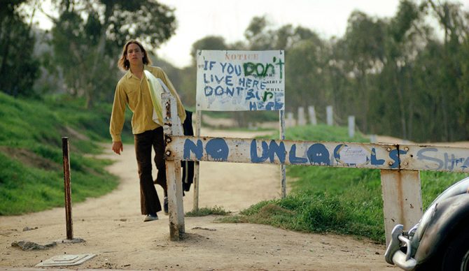 A surfer walks past signs at Sunset Cliffs