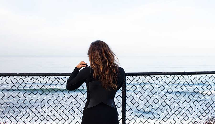 A woman looks at the ocean while wearing a wetsuit