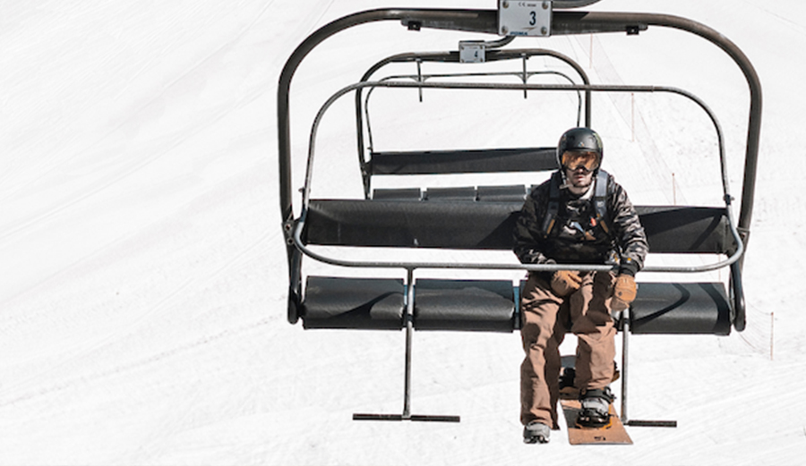 a man rides on a chairlift with his snowboard pointing forward.