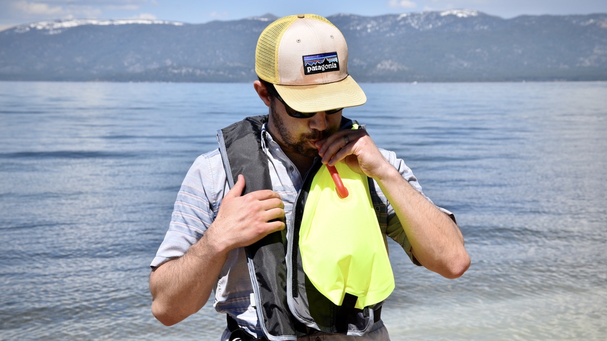 man inflating the BOTE inflatable vest life jacket in front of lake tahoe