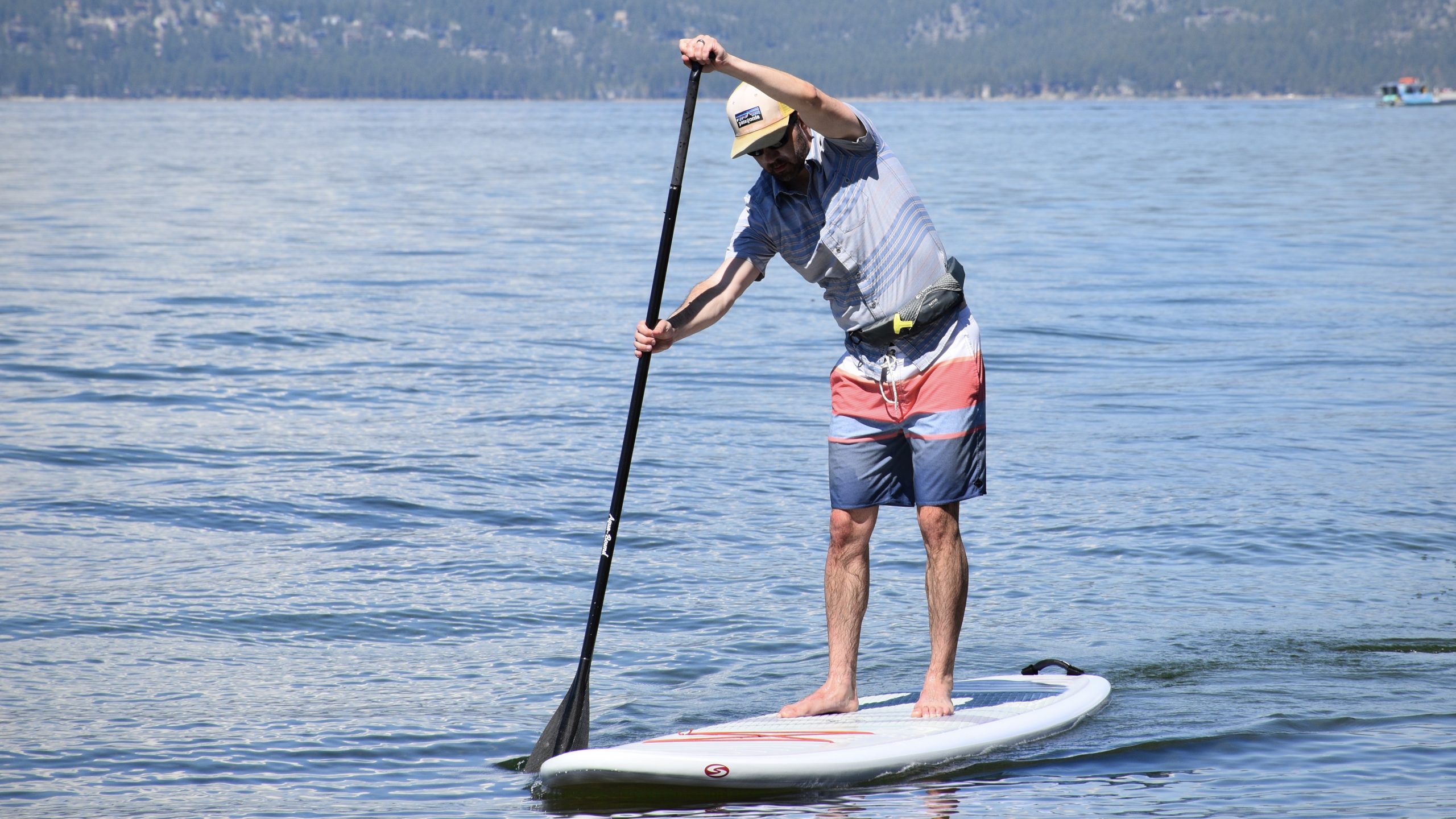 man paddle boarding on lake tahoe wearing the onyx m-16 inflatable belt life jacket