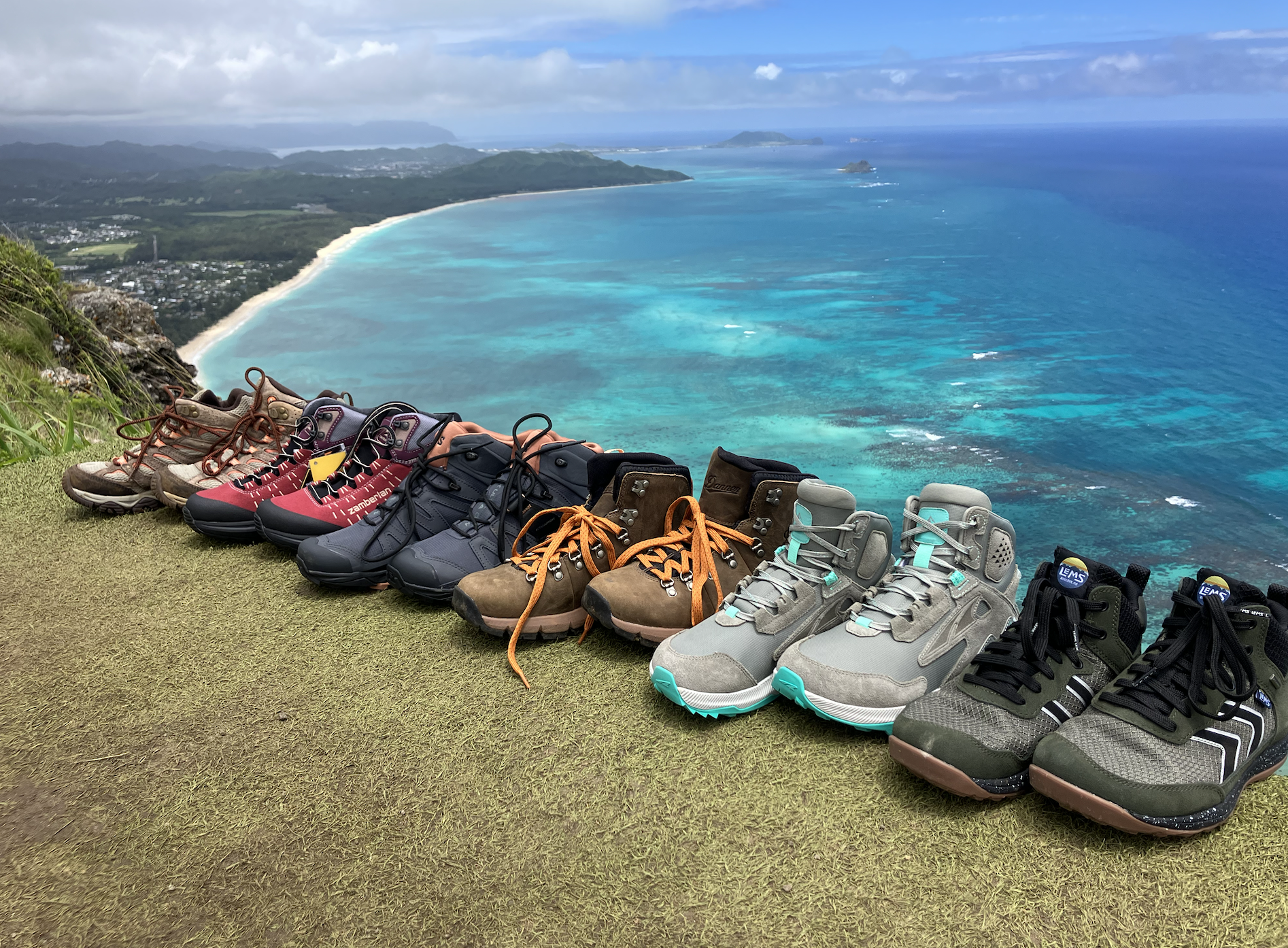 a bunch women's hiking boots lined up with the ocean in the background