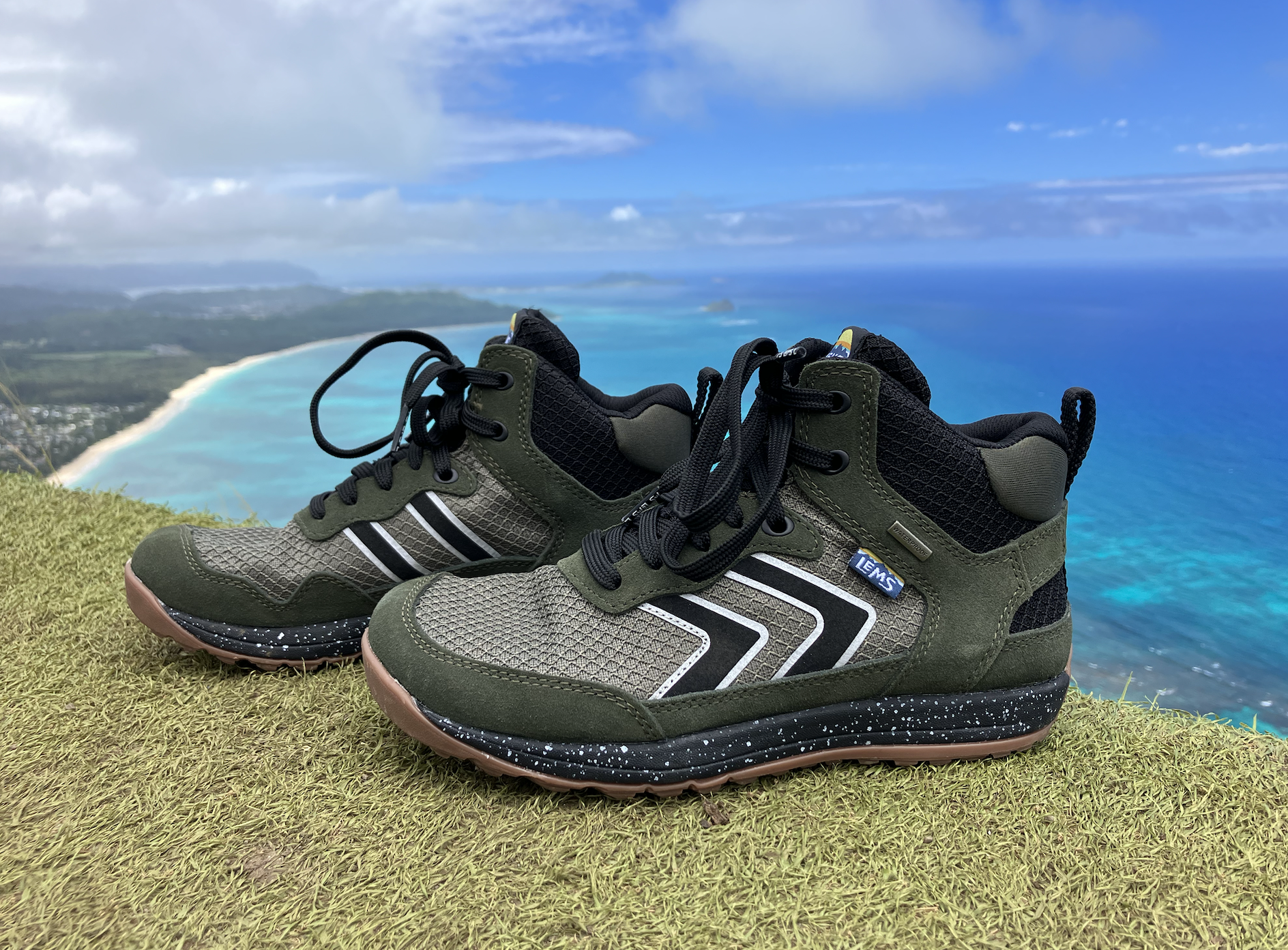 a close up of Lems Primal Pursuit Mid Waterproof hiking boots with the ocean in the background