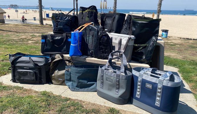 a photo of an assortment of totes, insulated coolers, and backpacks grouped together by the beach. These were the items we tested for our review of the best beach bags.