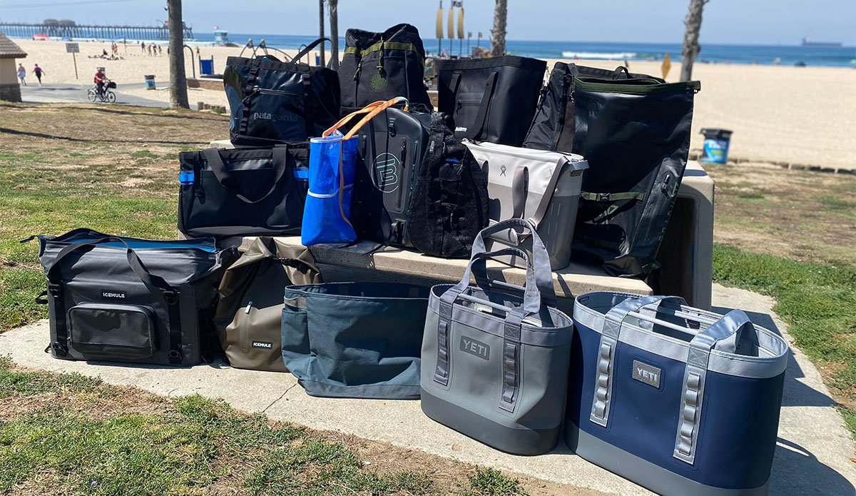 a photo of an assortment of totes, insulated coolers, and backpacks grouped together by the beach. These were the items we tested for our review of the best beach bags.