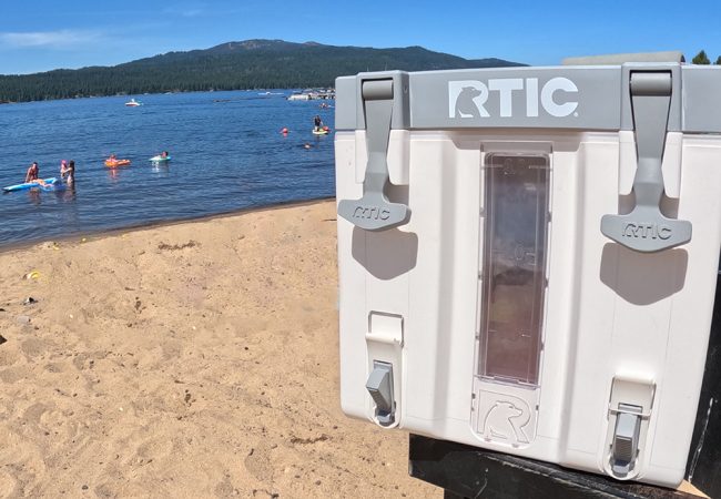 A view of the RTIC halftime water cooler next to a beach on a lake in the mountains.