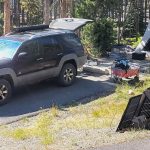 a campsite with a car unloading gear such as a tent, solar panel, wagon, and more for our review of the best car camping gear.
