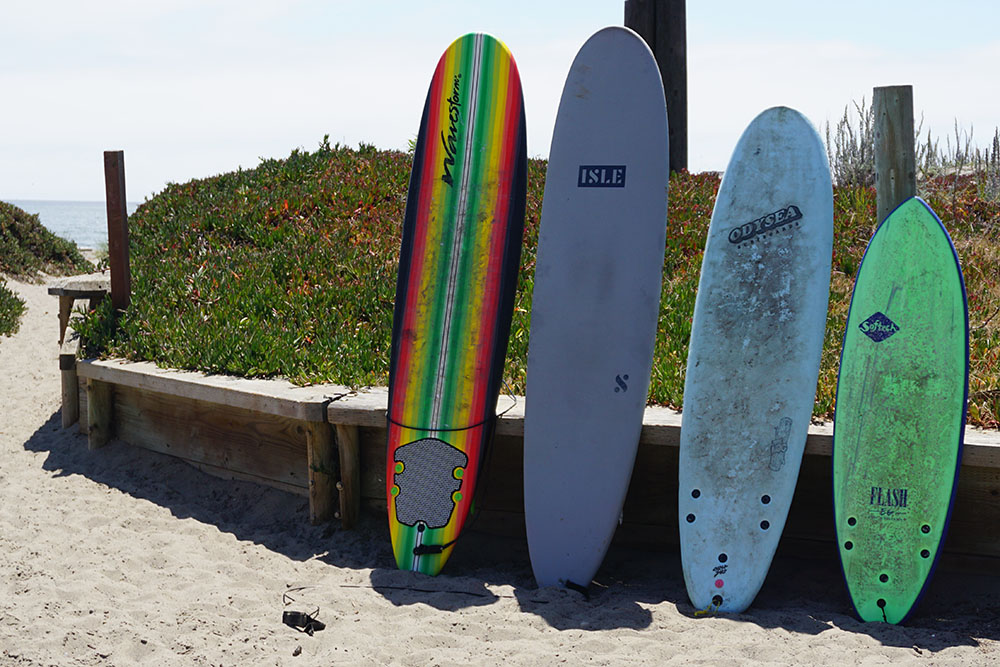 Four soft top surfboards of varying sizes, leaning up next to a sand dune on the beach for our test of the best soft top surfboards.