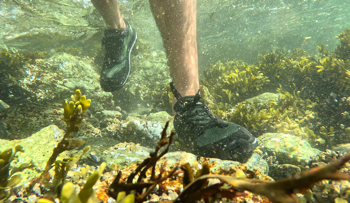 a man walks across a rocky ocean bottom in water shoes