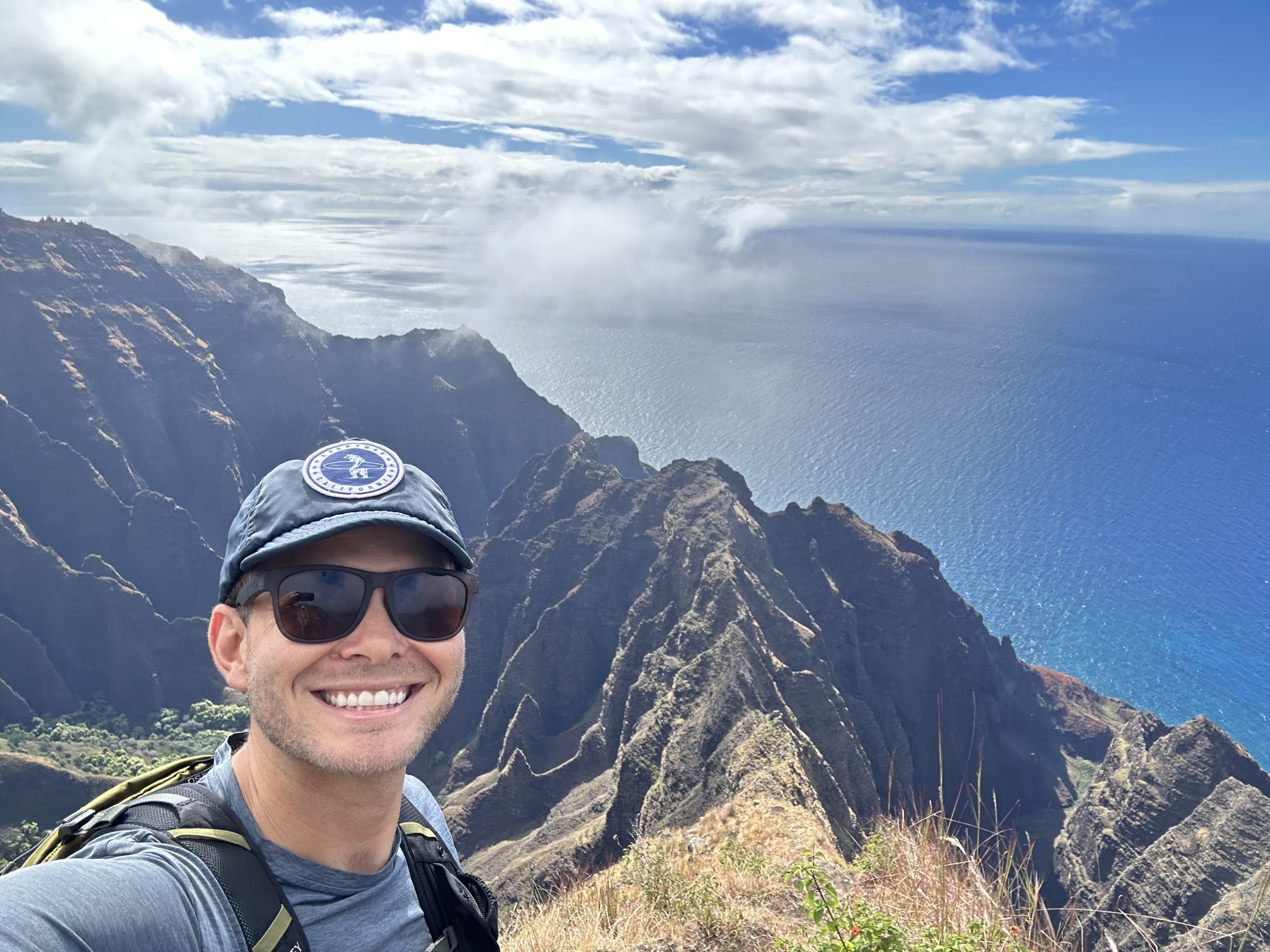 a man on a mountain over looking the ocean, wearing one of the surf hats we tested for this guide