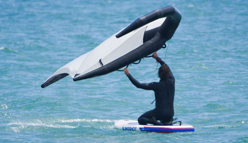 a man learning how to wing foil by starting on his knees on the slingshot ltf board in the water.