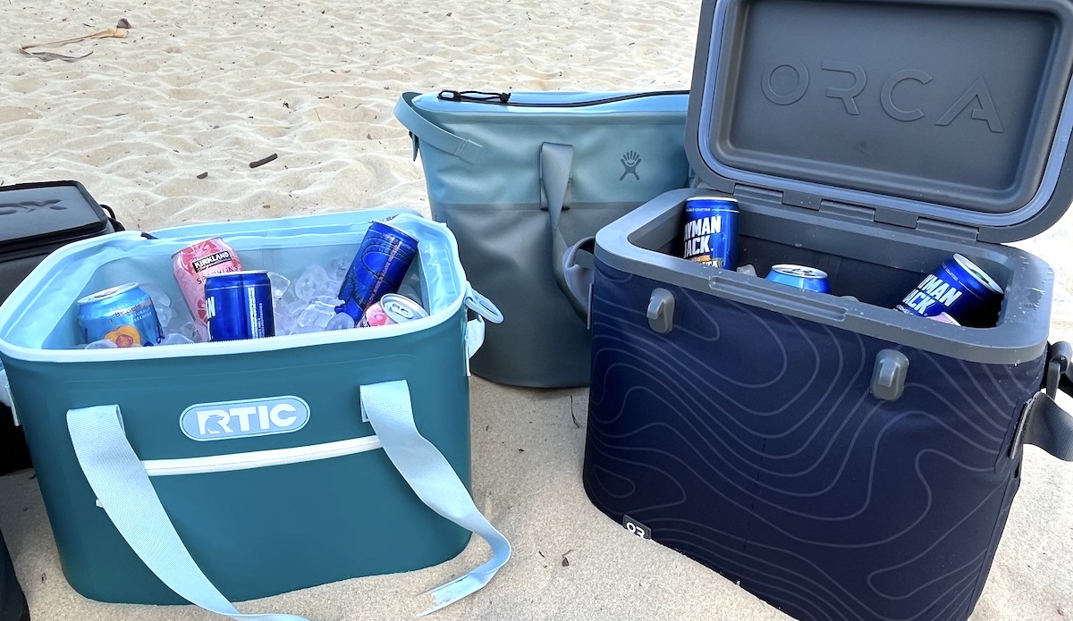 a variety of soft coolers sitting on the beach open with drinks in them
