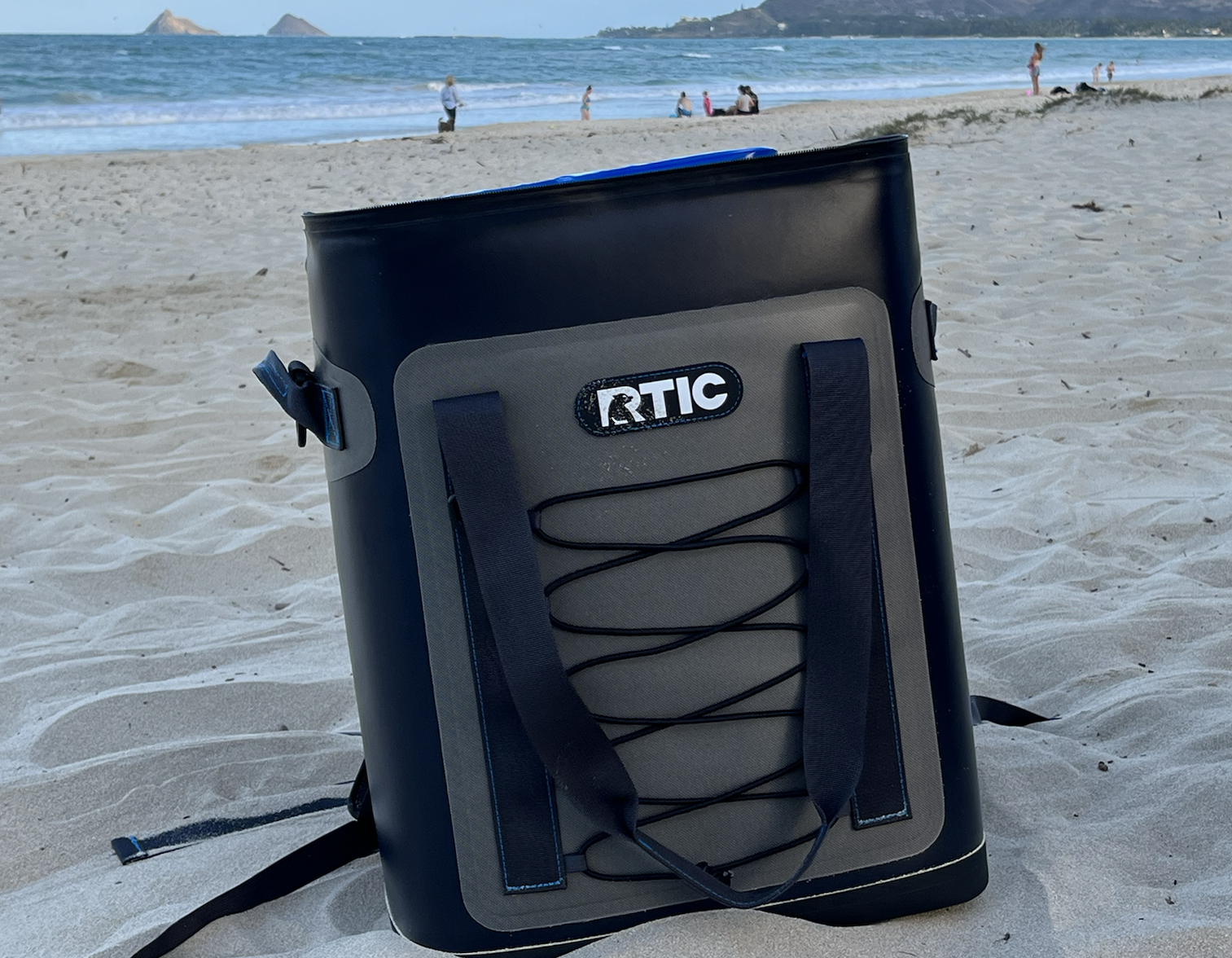 RTIC Backpack Cooler sitting on the beach with islands in the background
