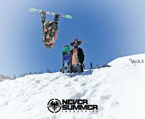 A snowboarder inverted in the air over a cutout of a cowboy on a sunny bluebird day.