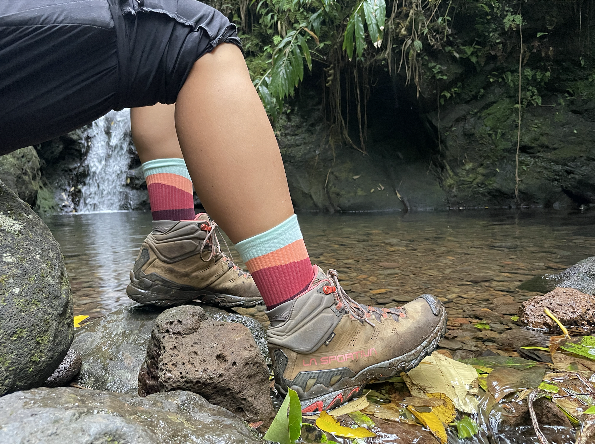 two feet with socks and boots on the edge of a pond