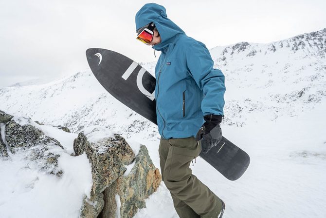 a snowboarder hikes the ridgeline of a mountain while holding his snowboard