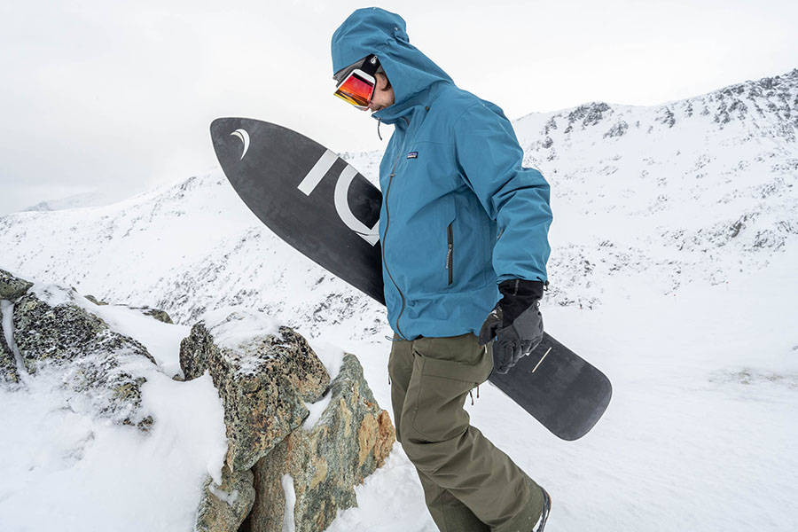 a snowboarder hikes the ridgeline of a mountain while holding his snowboard
