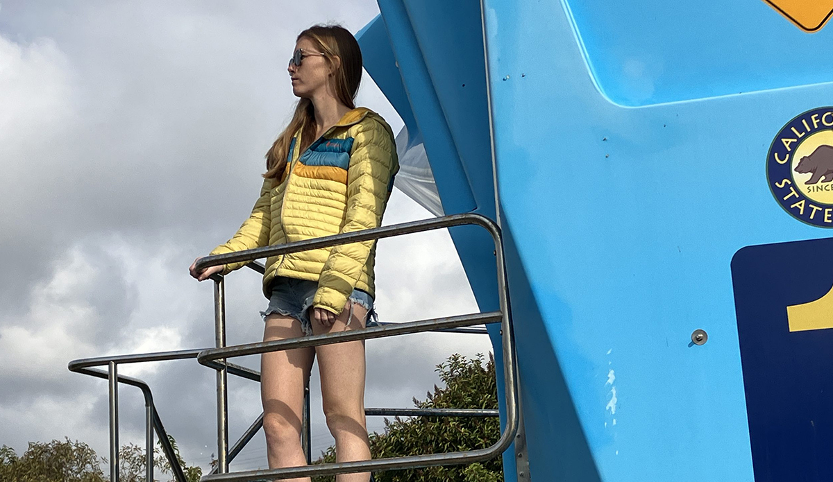a woman stands on a lifeguard tower wearing The Cotopaxi Fuego Down Hoodie