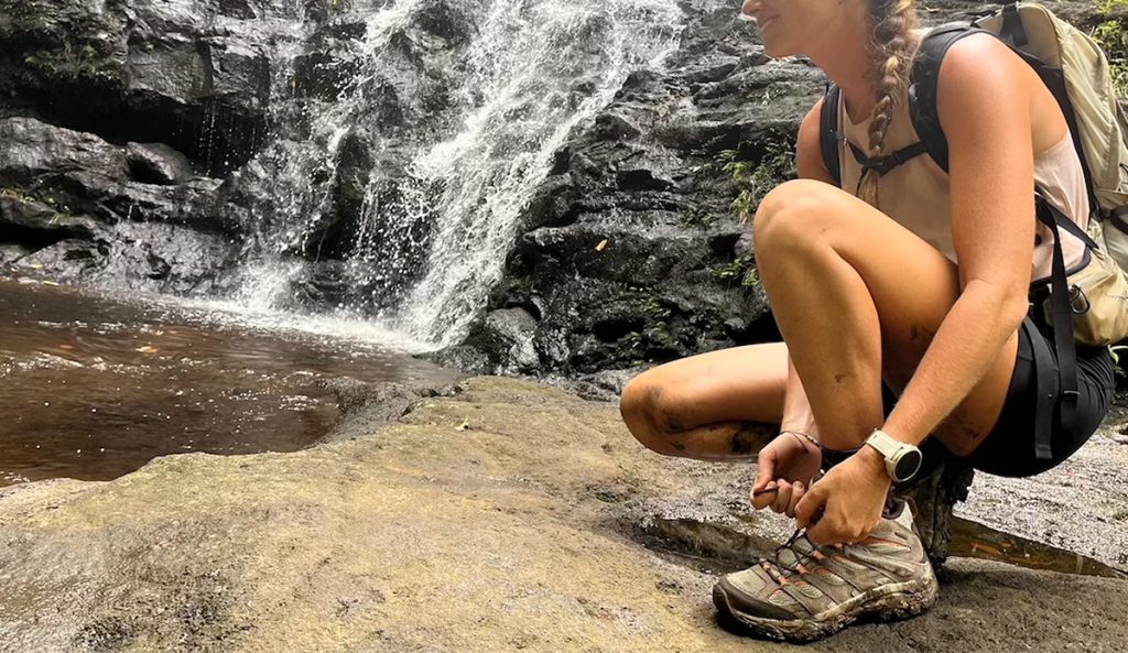 a woman ties her shoes next to a waterfall