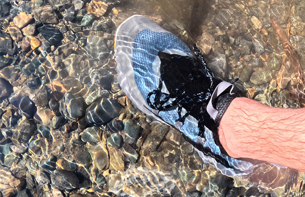 looking downward at the Danner Rivercomber water shoes while walking through a river with a rocky bottom.