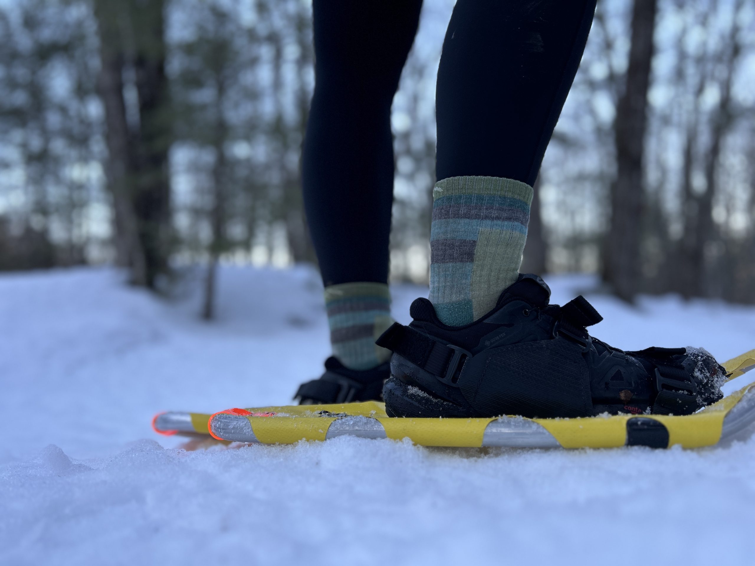 A women testing a pair of yellow snowshoes on a flat trail