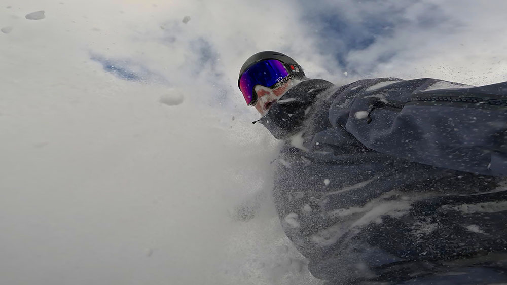 a snowboarder riding through powder, action shot wearing dragon nfx mag infared goggles