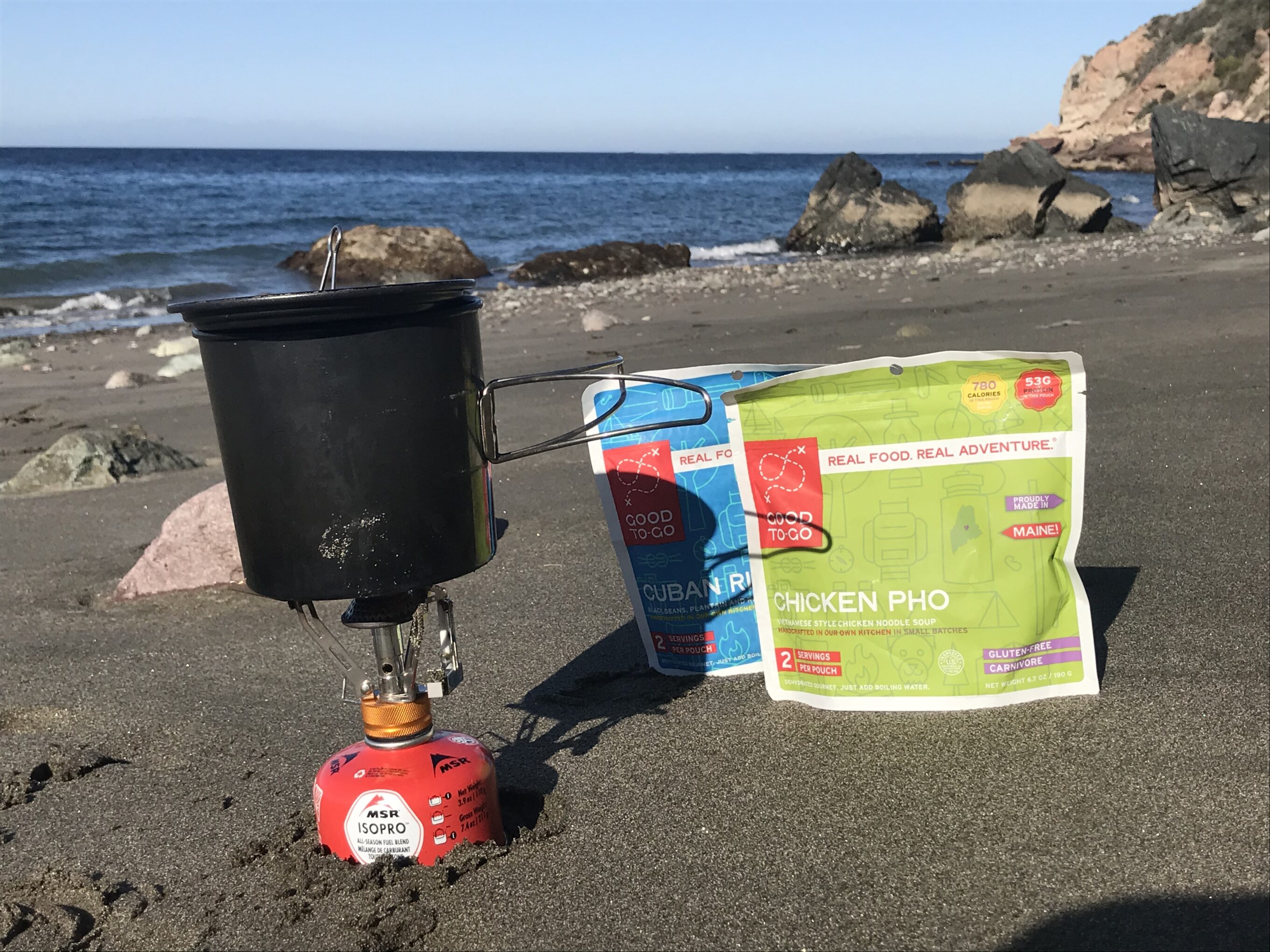 two backpacking meals and stove on the beach