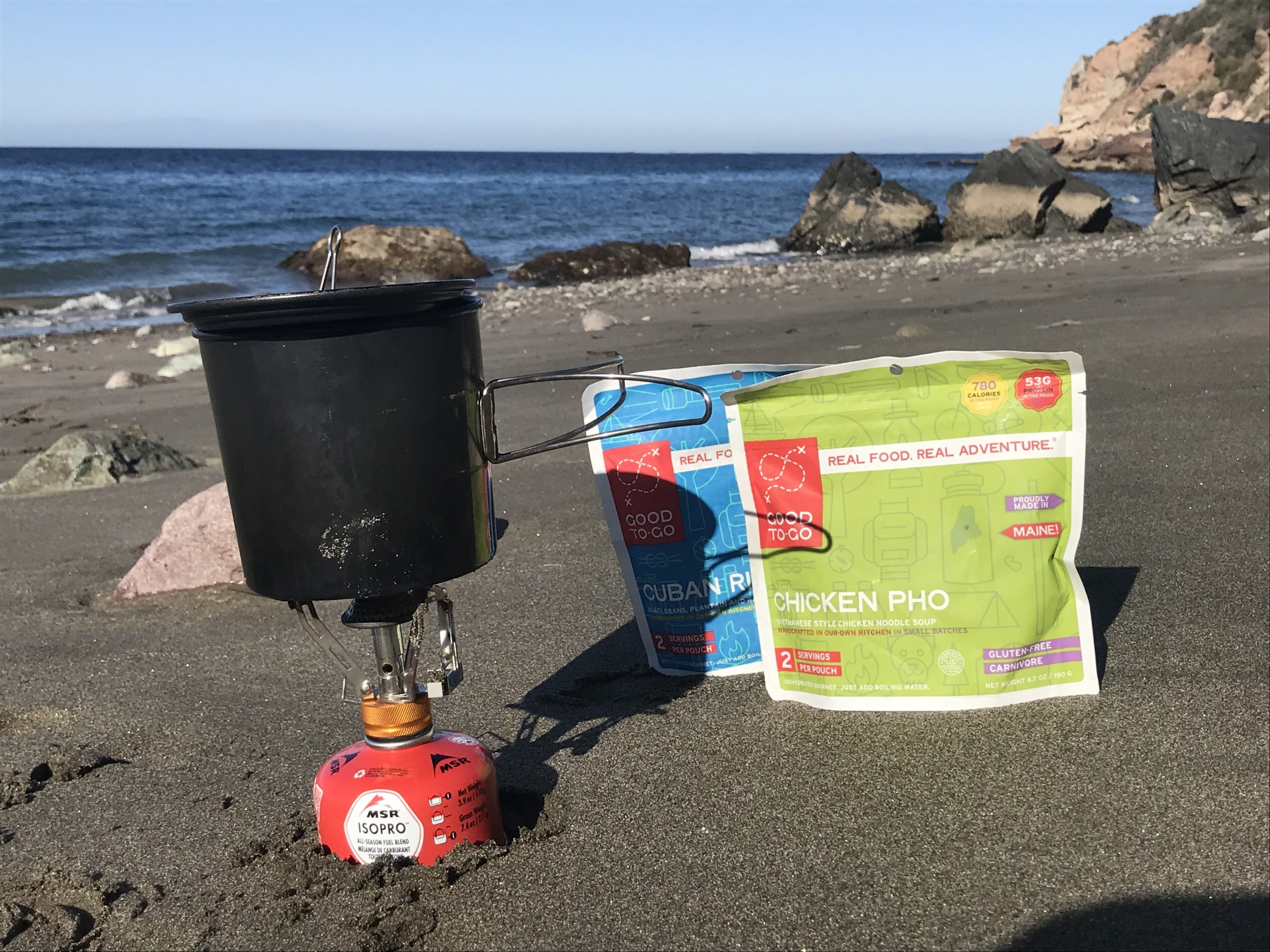 two backpacking meals and stove on the beach