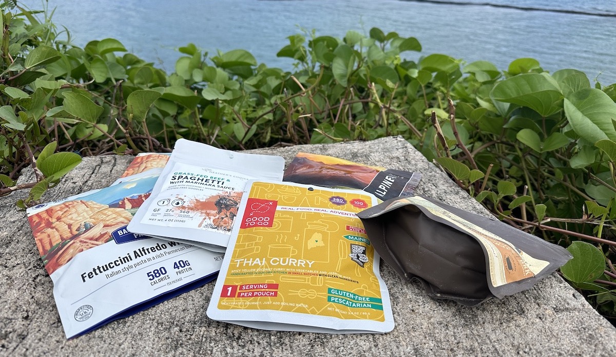 a variety of backpacking meals with water in the background