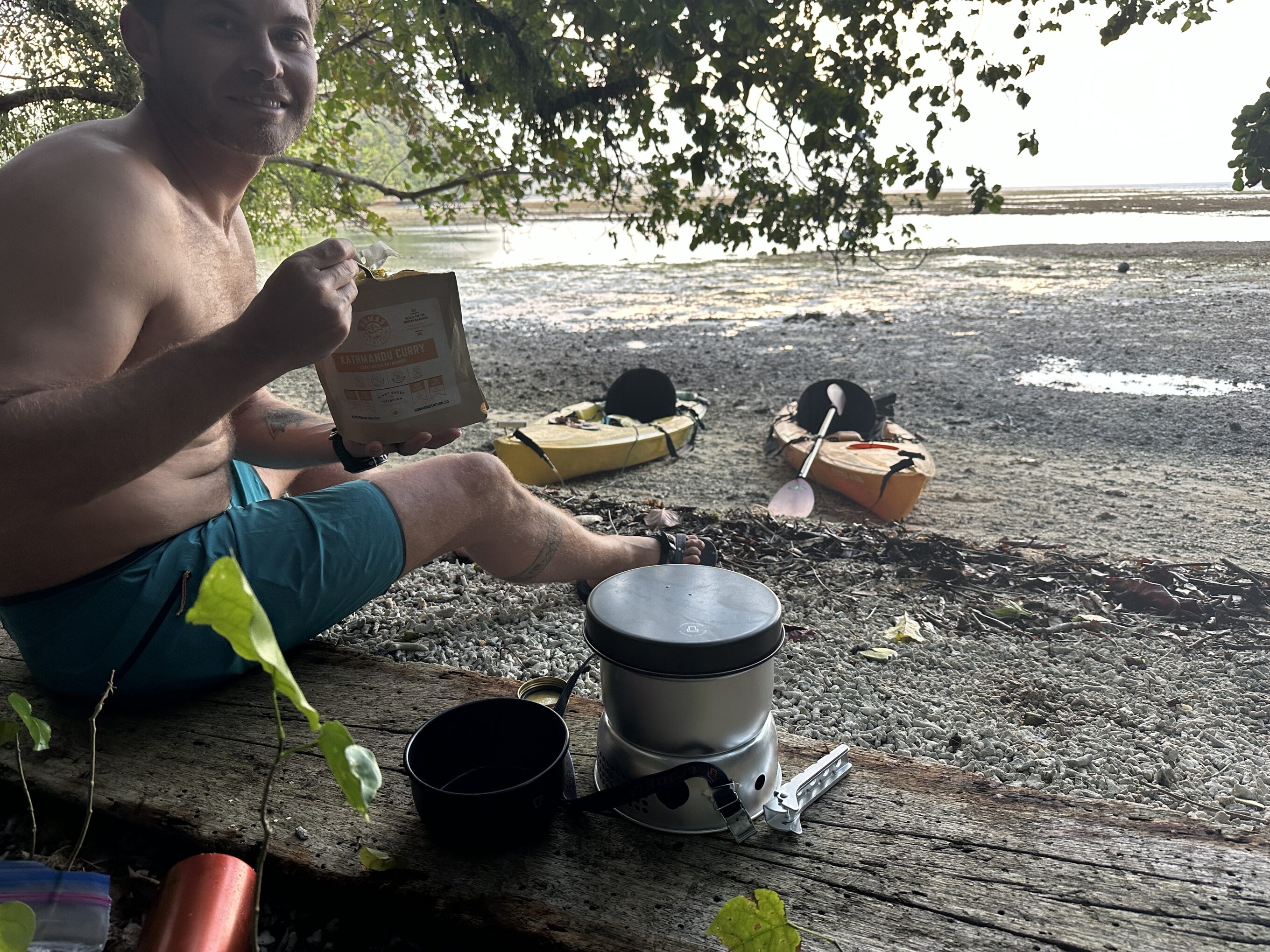 man eating backpacking meals at the beach that were cooked in a backpacking stove