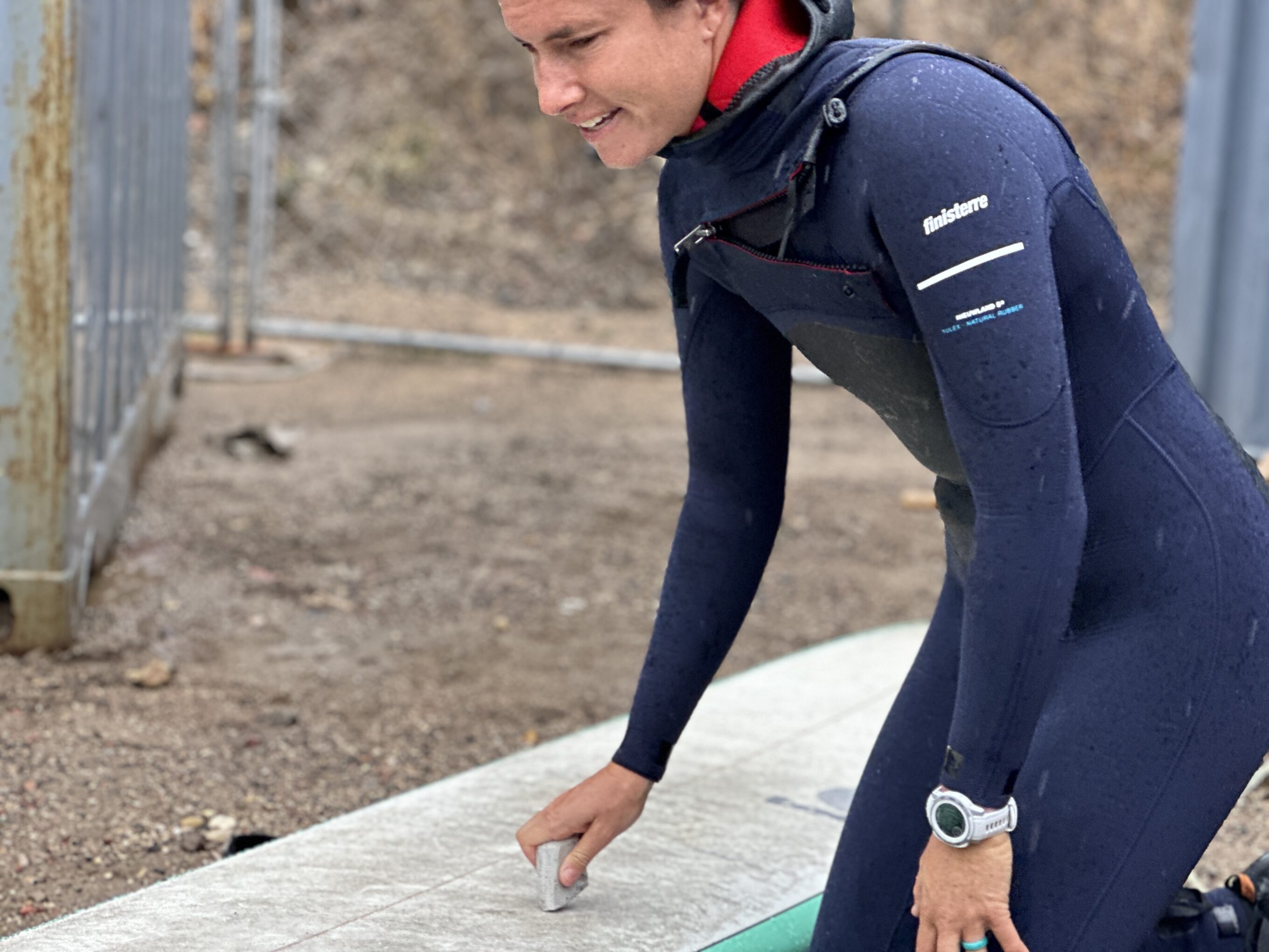 woman waxing down a surfboard in a wetsuit