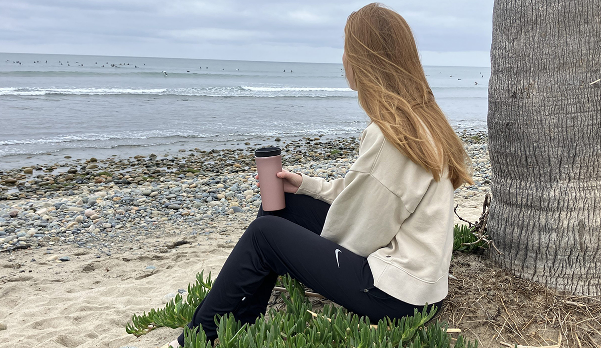 a woman holding an insulated coffee mug while looking at the surf at the beach