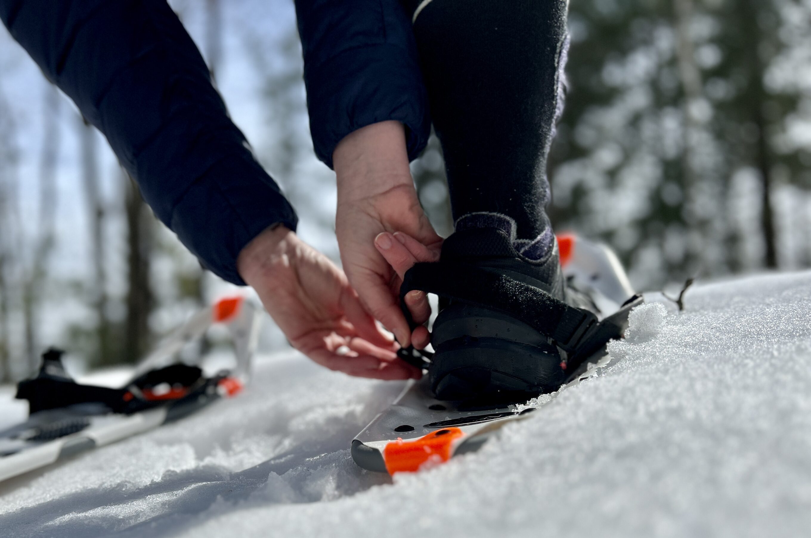 A view of a woman's hands adjusting the bindings on the Dion 121 snowshoes