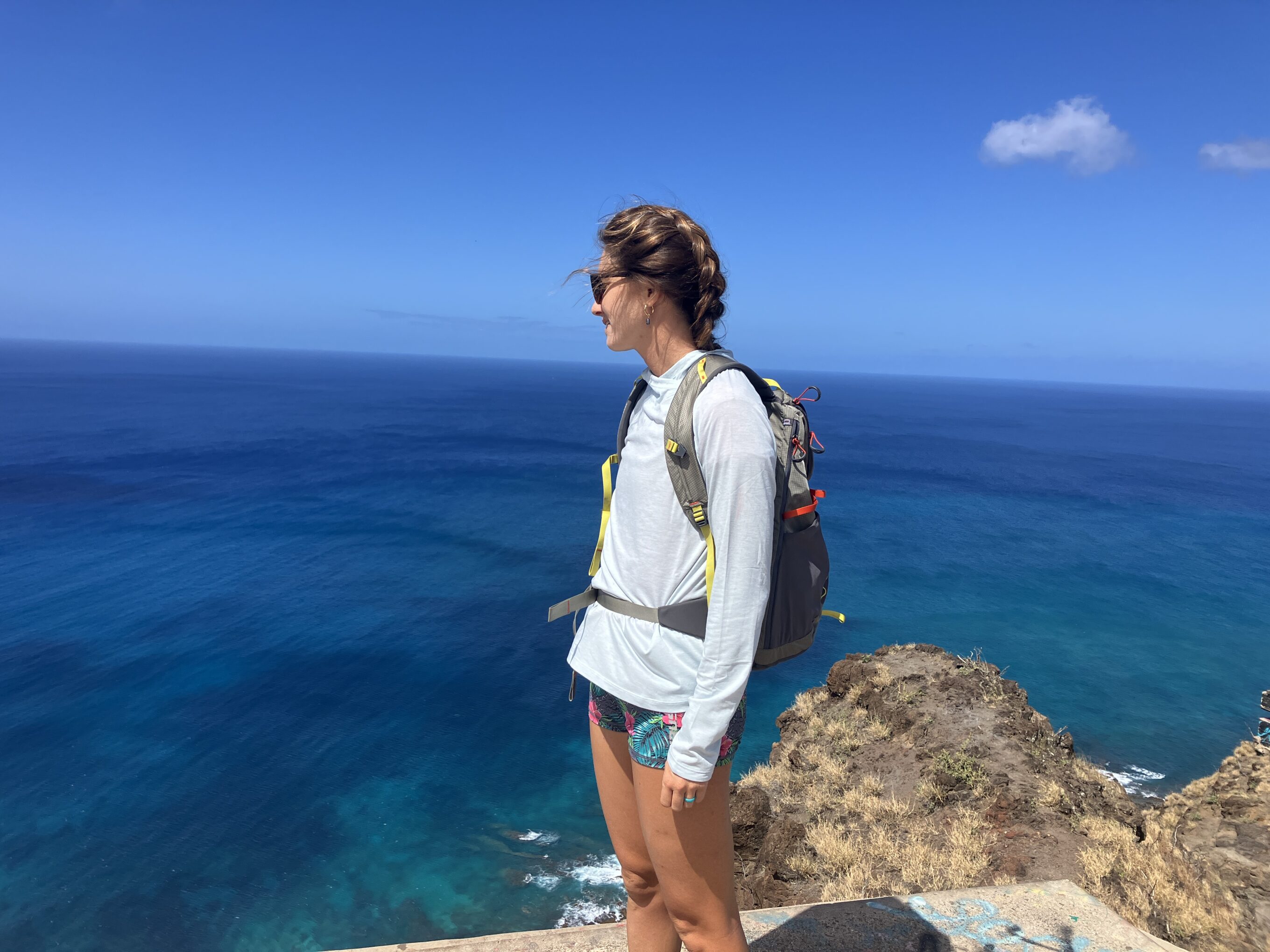 a woman standing on a cliff overlooking the ocean in a sun shirt