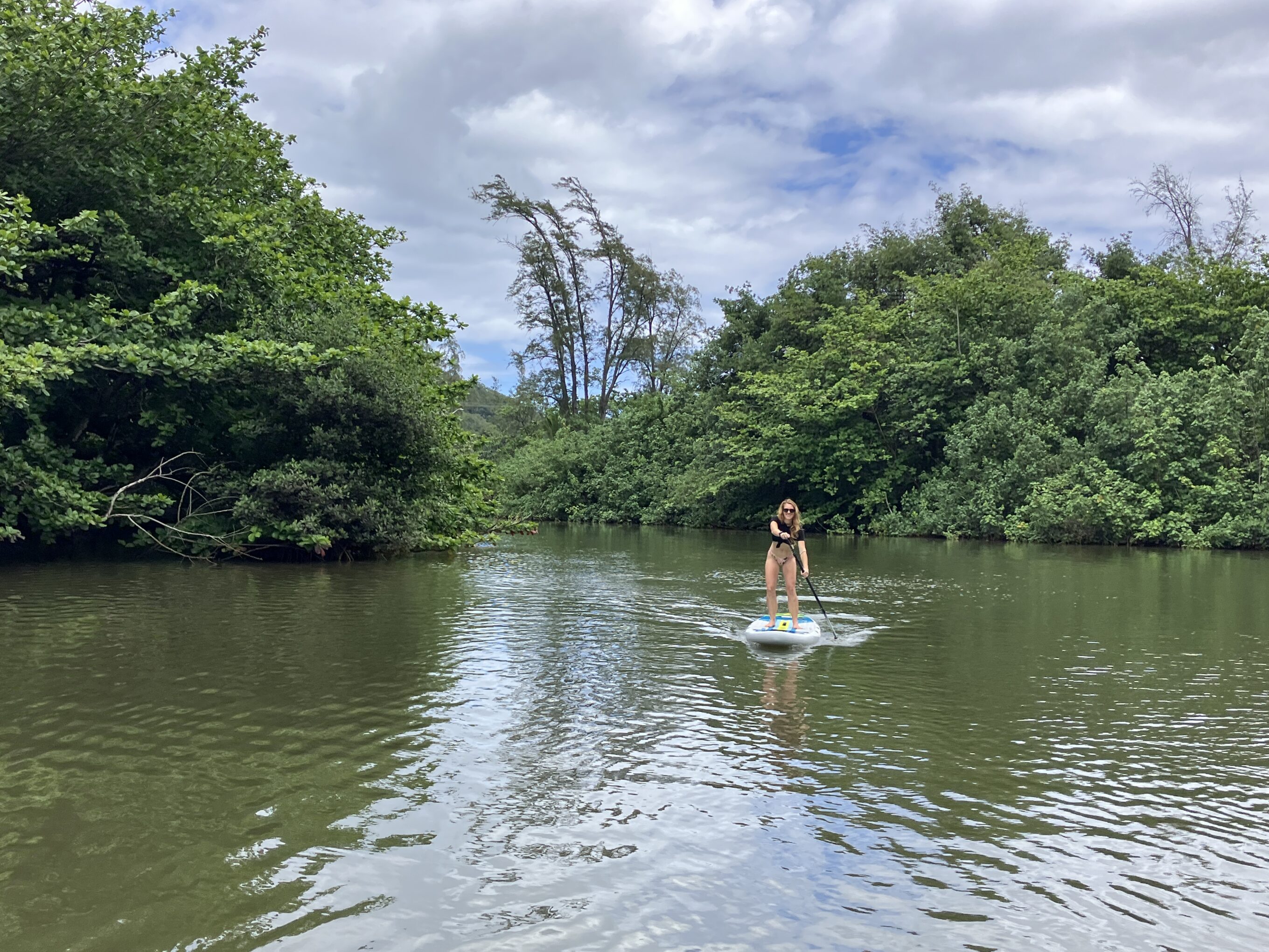 a far away photo of a woman stand up paddling on a picturesque lagoon