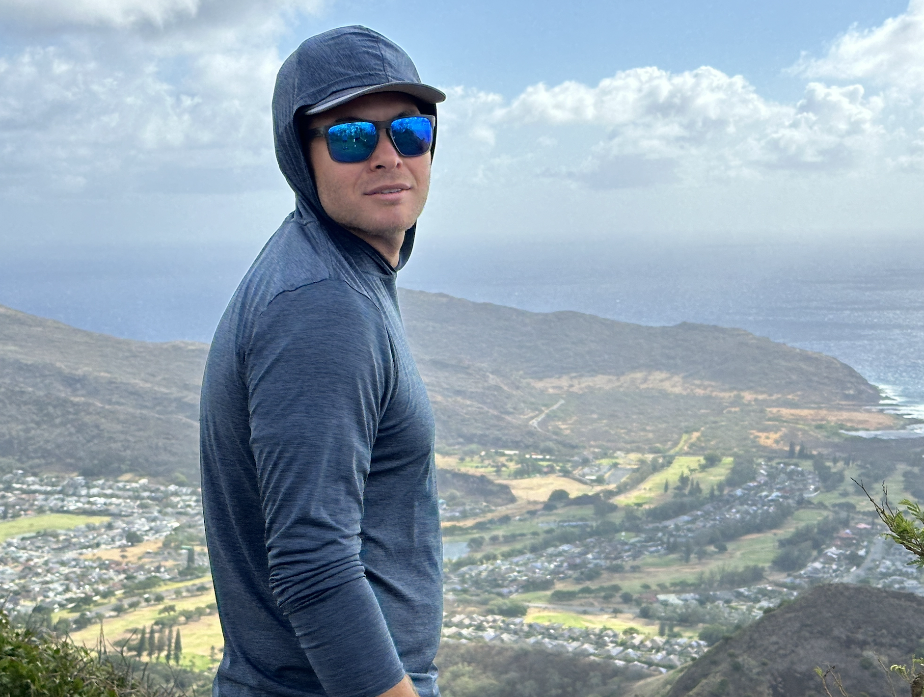 a man wearing a hooded sun shirt with the ocean in the background