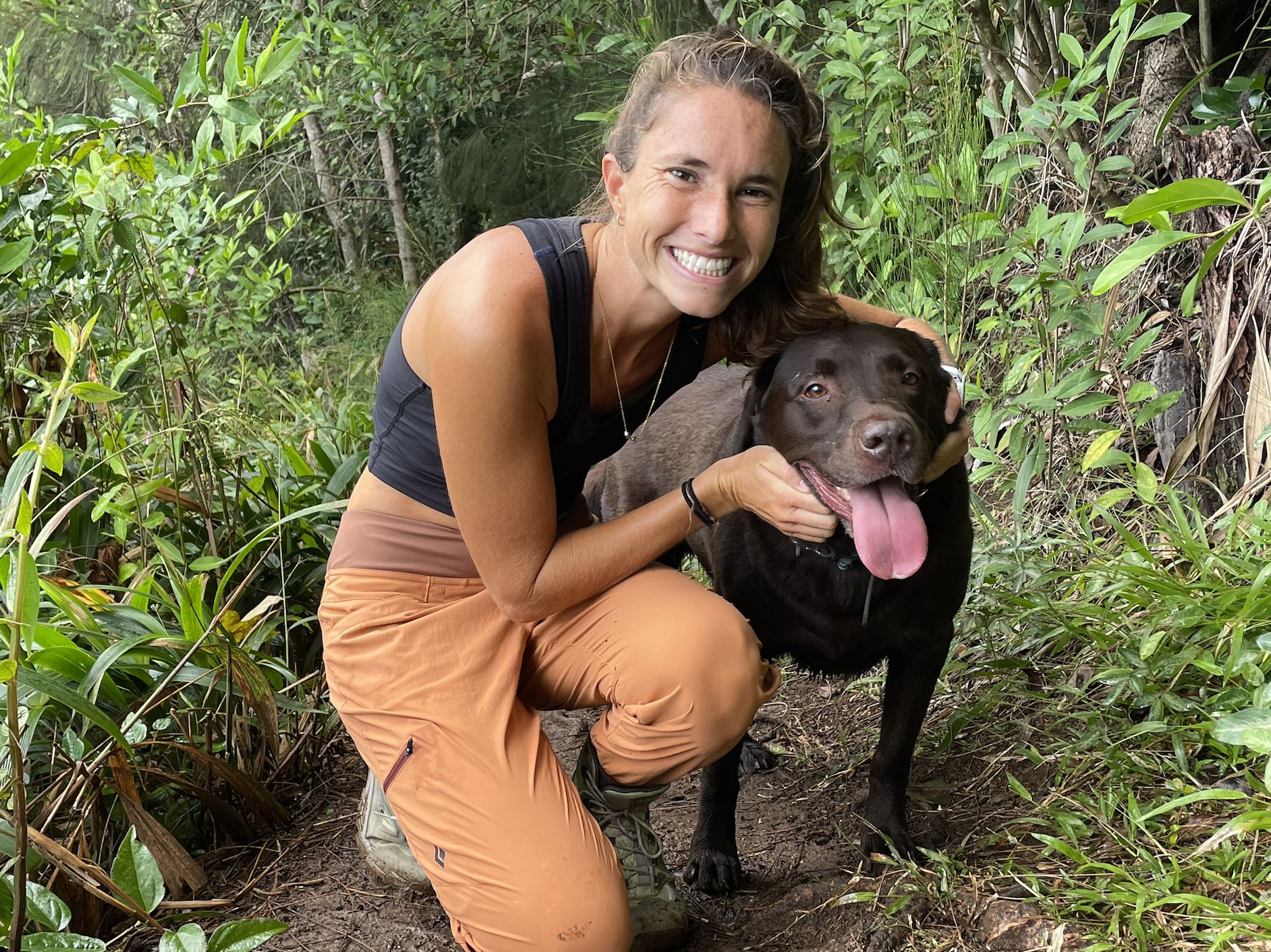 a woman in hiking pants and a dog in the forest