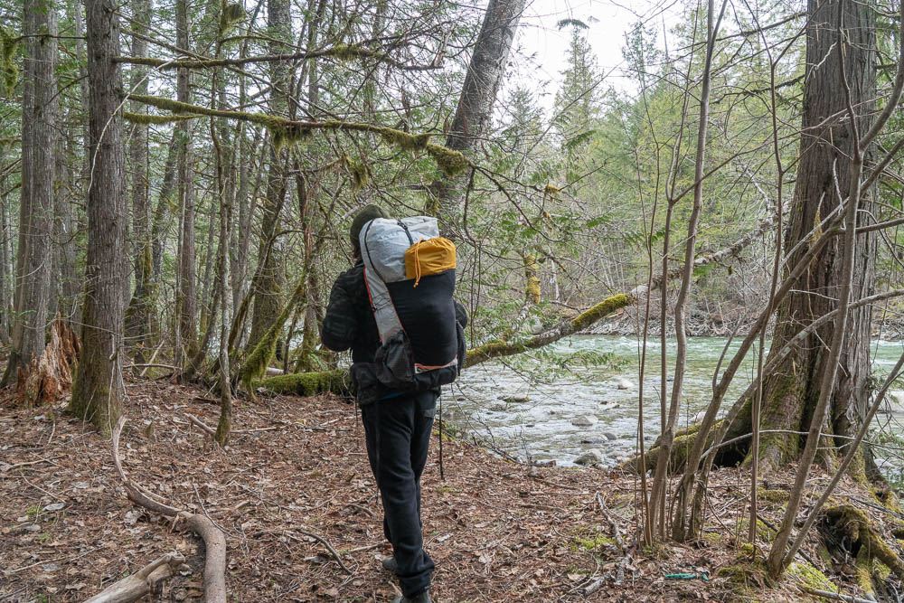 a backpacker hiking next to a river while testing out the best backpacks to review
